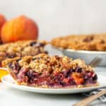 A slice of blueberry peach pie served on a white plate.