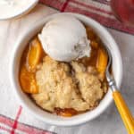 A bowl of gluten free peach cobbler topped with a scoop of vanilla ice cream.