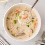A spoon scooping up a bite of creamy rice and mushroom soup from a bowl.