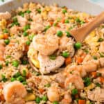 A wooden spoon scooping a serving of shrimp and chicken fried rice from the skillet.