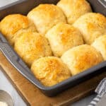 A pan of freshly baked gluten free dinner rolls cooling on a wooden cutting board.