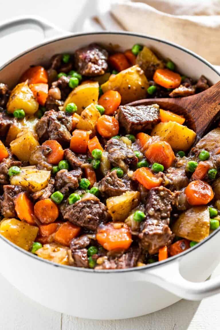 A dutch oven filled with beef stew showing chunks of beef, carrots, potatoes and peas.