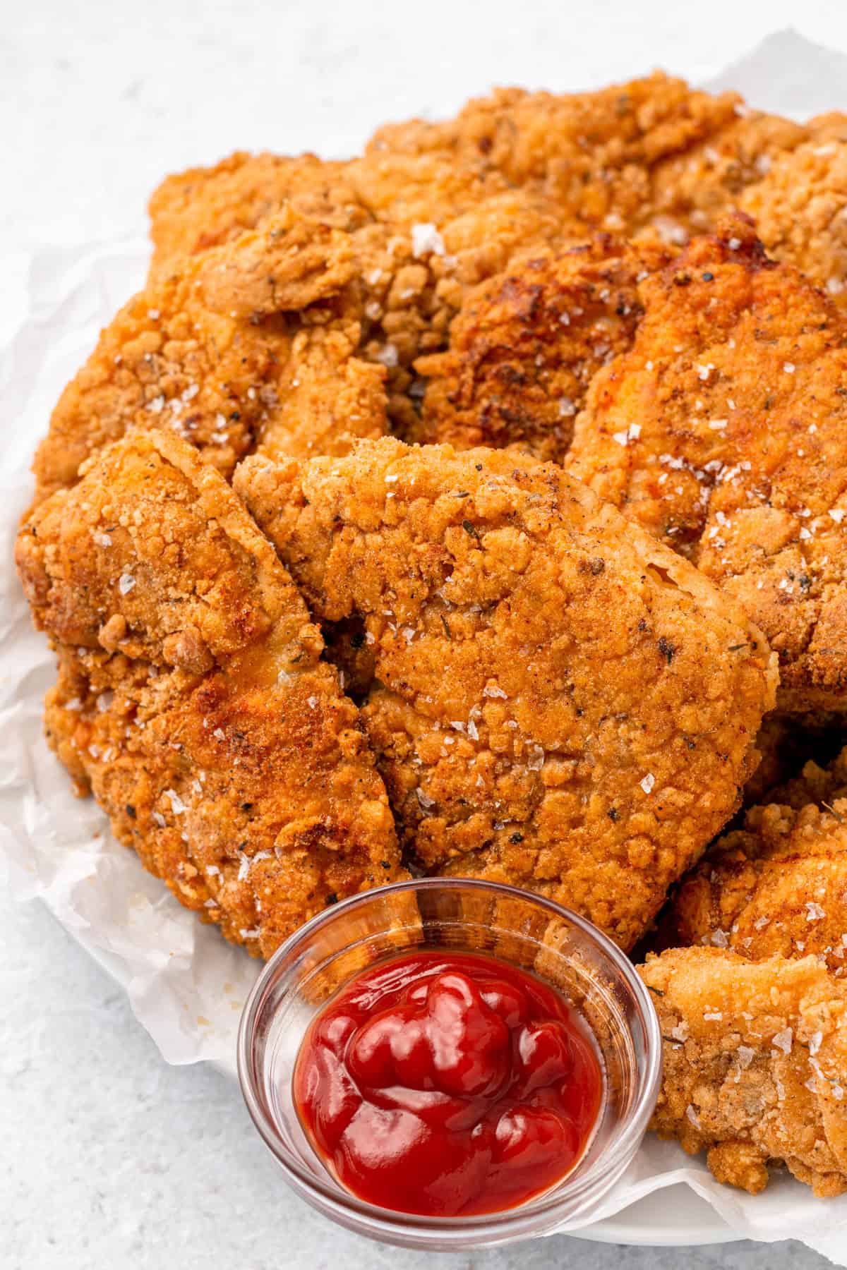 A plate of gluten free fried chicken with a small dish of ketchup.