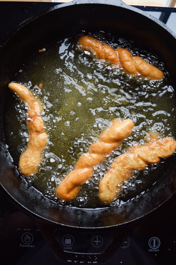 Four gluten free cinnamon twist donuts frying in a dutch oven pot.