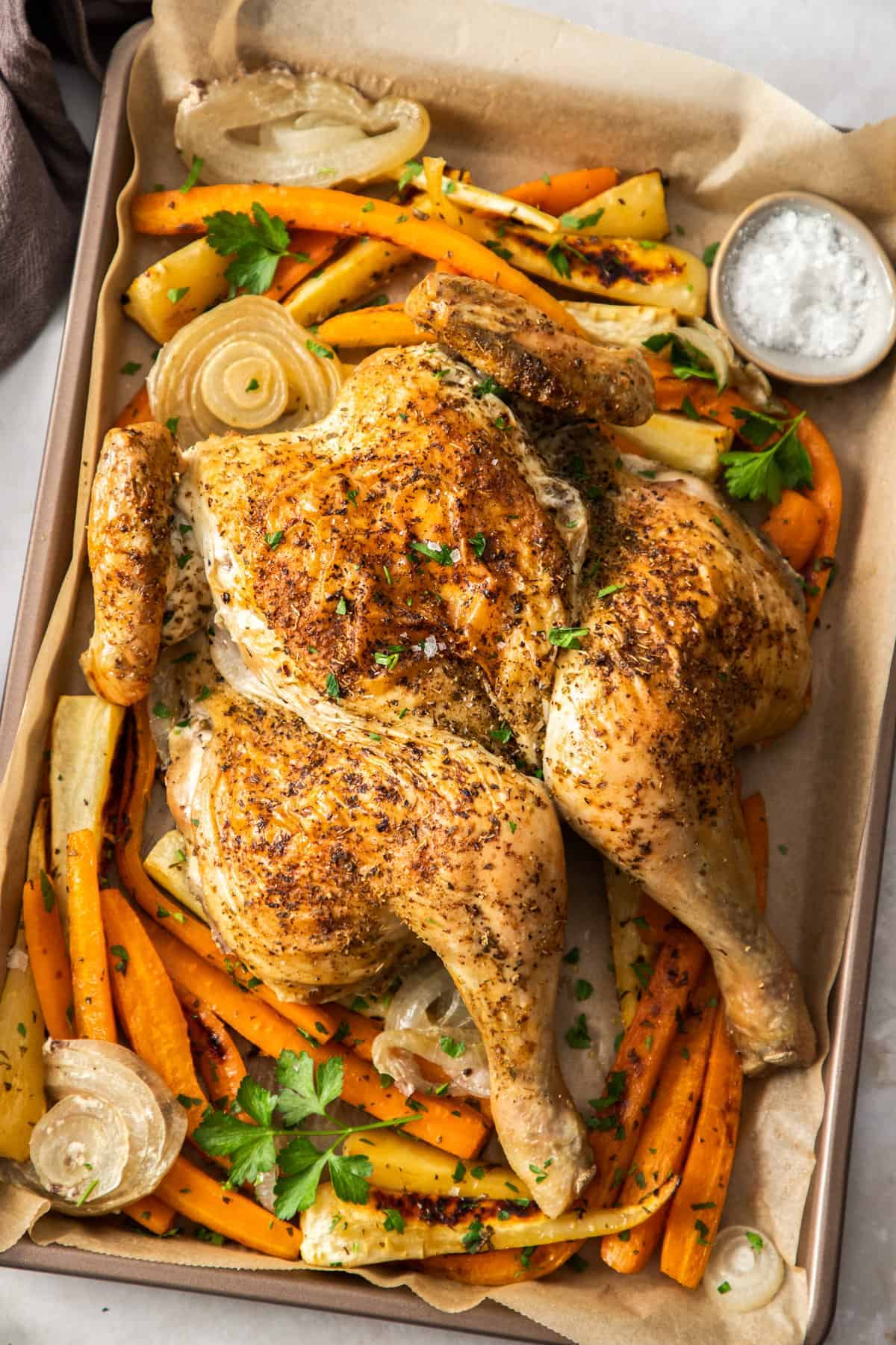 A spatchcock roasted chicken on a baking tray with onions and carrots.