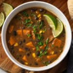 A bowl of black bean and sweet potato soup garnished with cilantro and lime wedges.