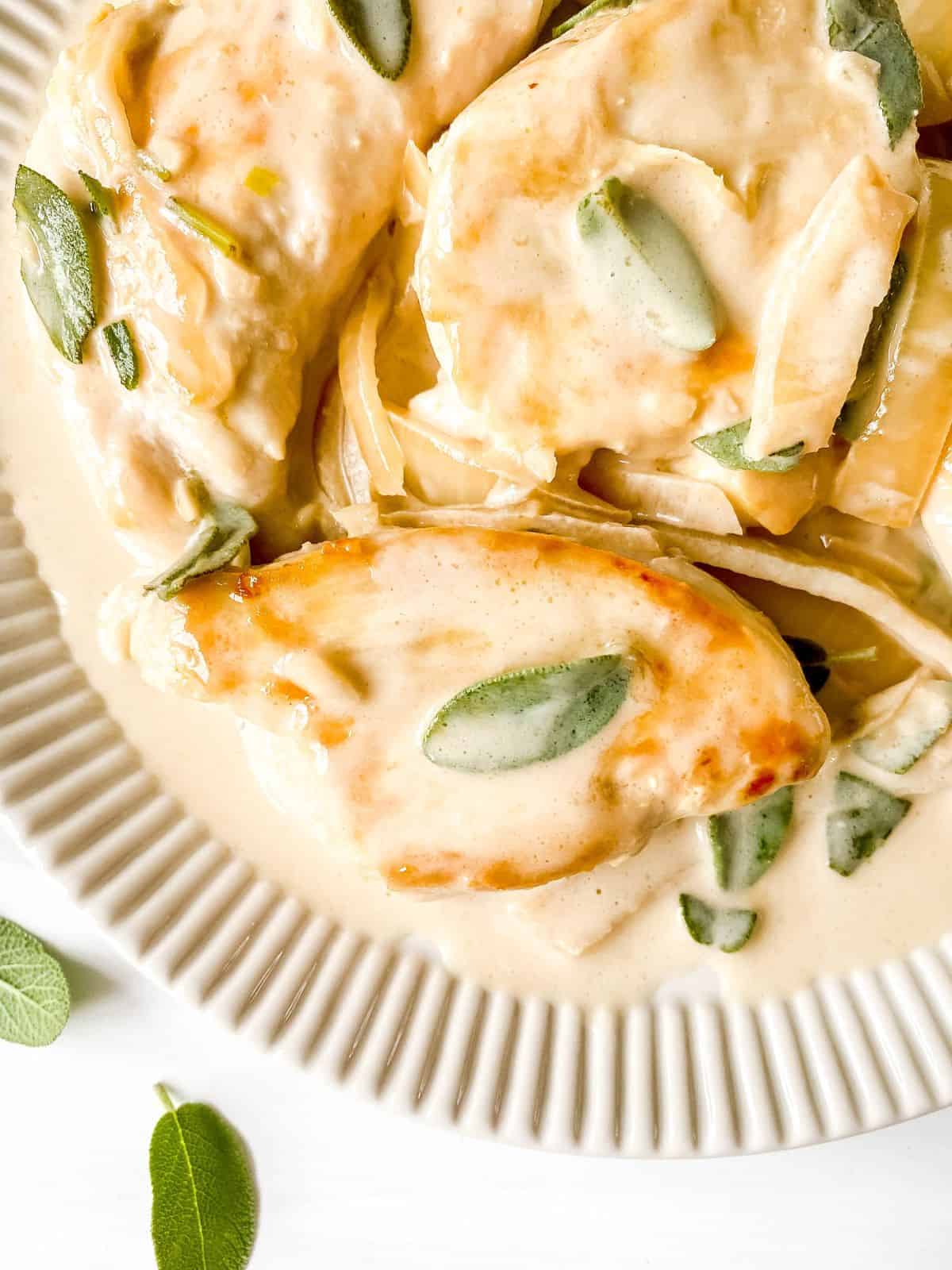 Creamy chicken with fresh sage leaves on a serving platter.