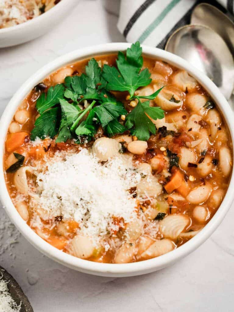 A bowl of gluten free pasta fagioli topped with Parmesan cheese and parsley.