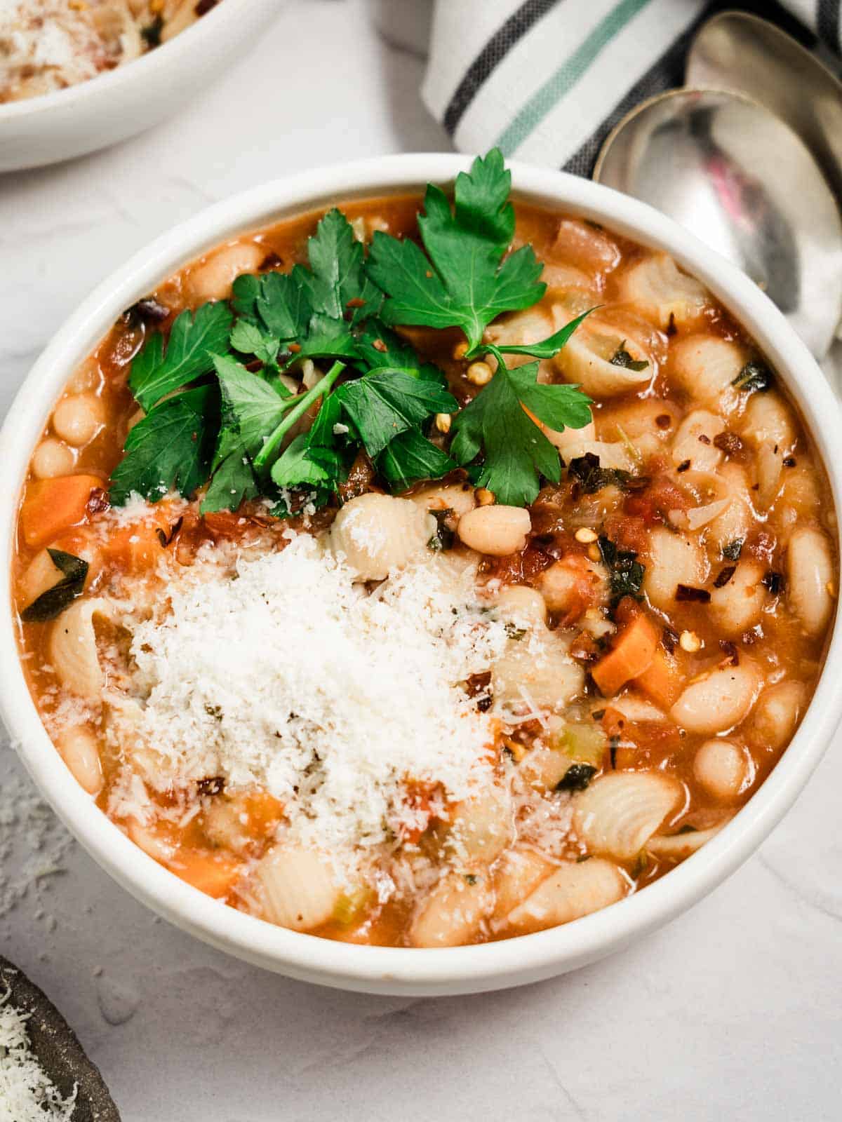 A bowl of pasta fagioli topped with parmesan cheese and parsley.