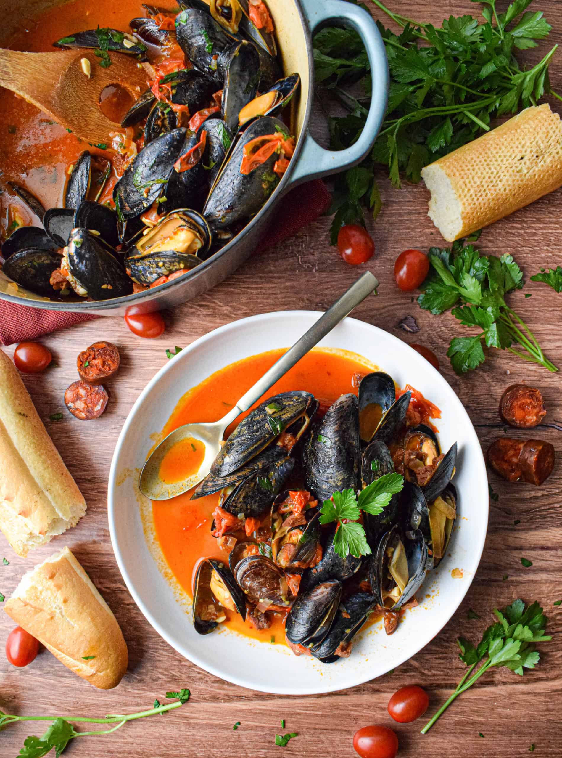 A bowl of mussels and chorizo on a wood table.