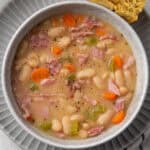 A bowl of white bean and ham soup served with a piece of cornbread.