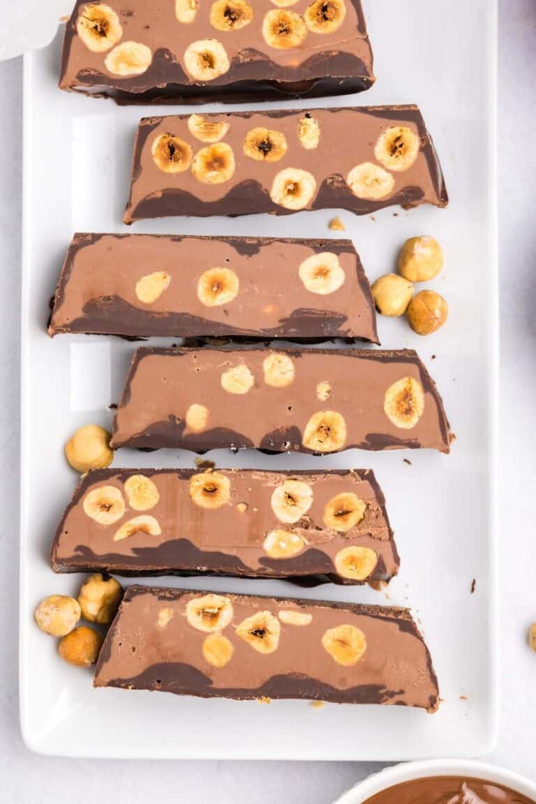 A chocolate hazelnut torrone sliced and laid on a plate showing the interior layers of chocolate and whole hazelnuts.