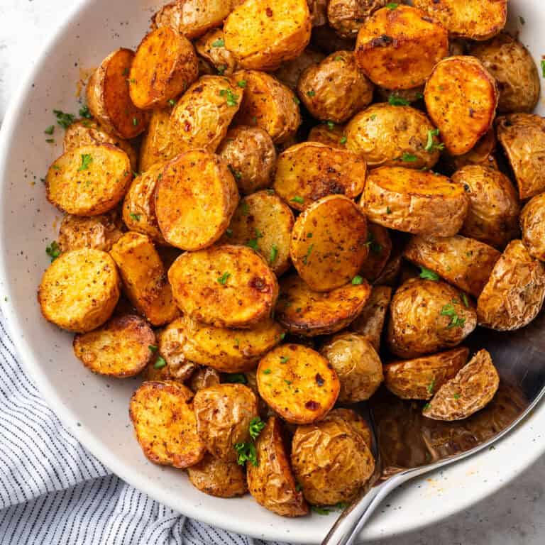 A serving spoon scooping into a bowl of golden brown roasted baby potatoes.