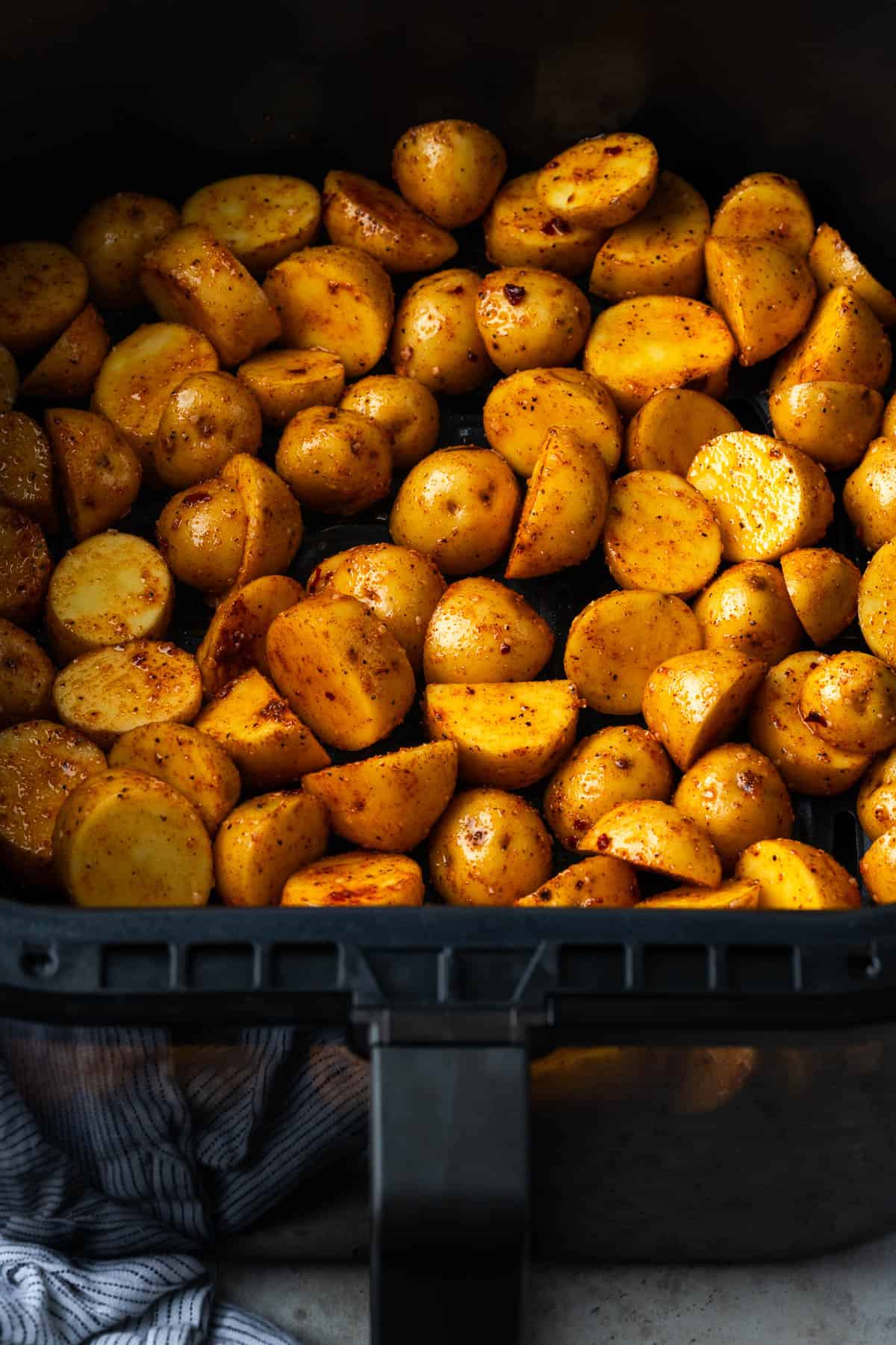 Uncooked baby potatoes spread in a single layer in the air fryer drawer.