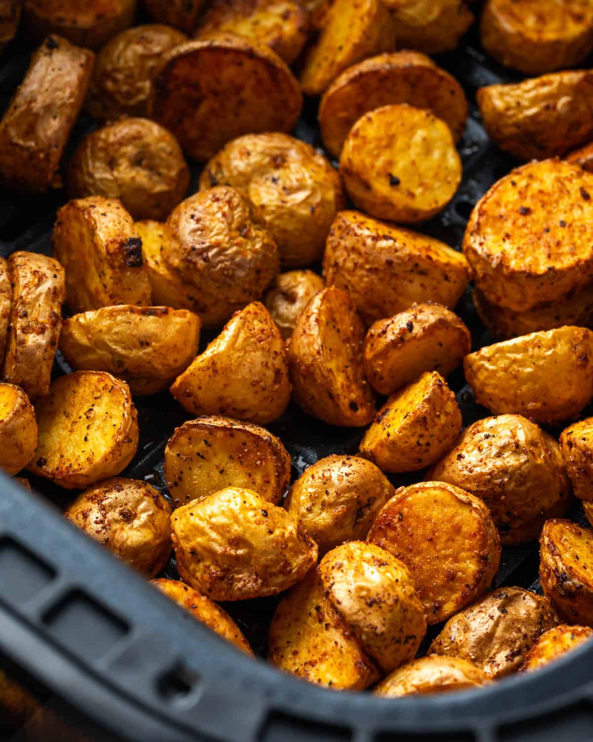 Golden brown seasoned potatoes in an air fryer drawer.