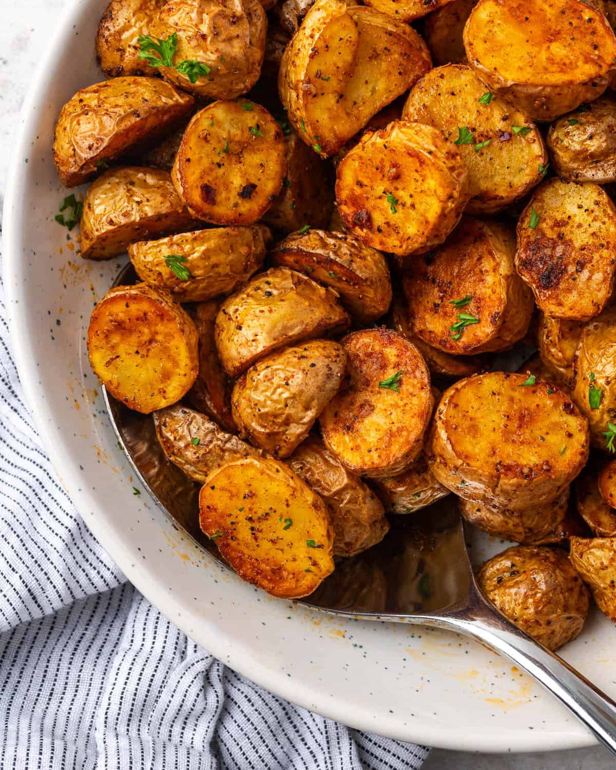 A serving spoon scooping up some baked baby potatoes from a bowl.
