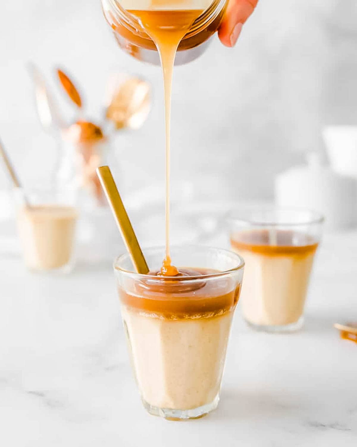 Salted caramel sauce being poured over a glass filled with butterscotch pudding. 