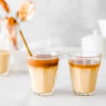 Two glasses of butterscotch budino topped with salted caramel sauce sitting on a marble counter.