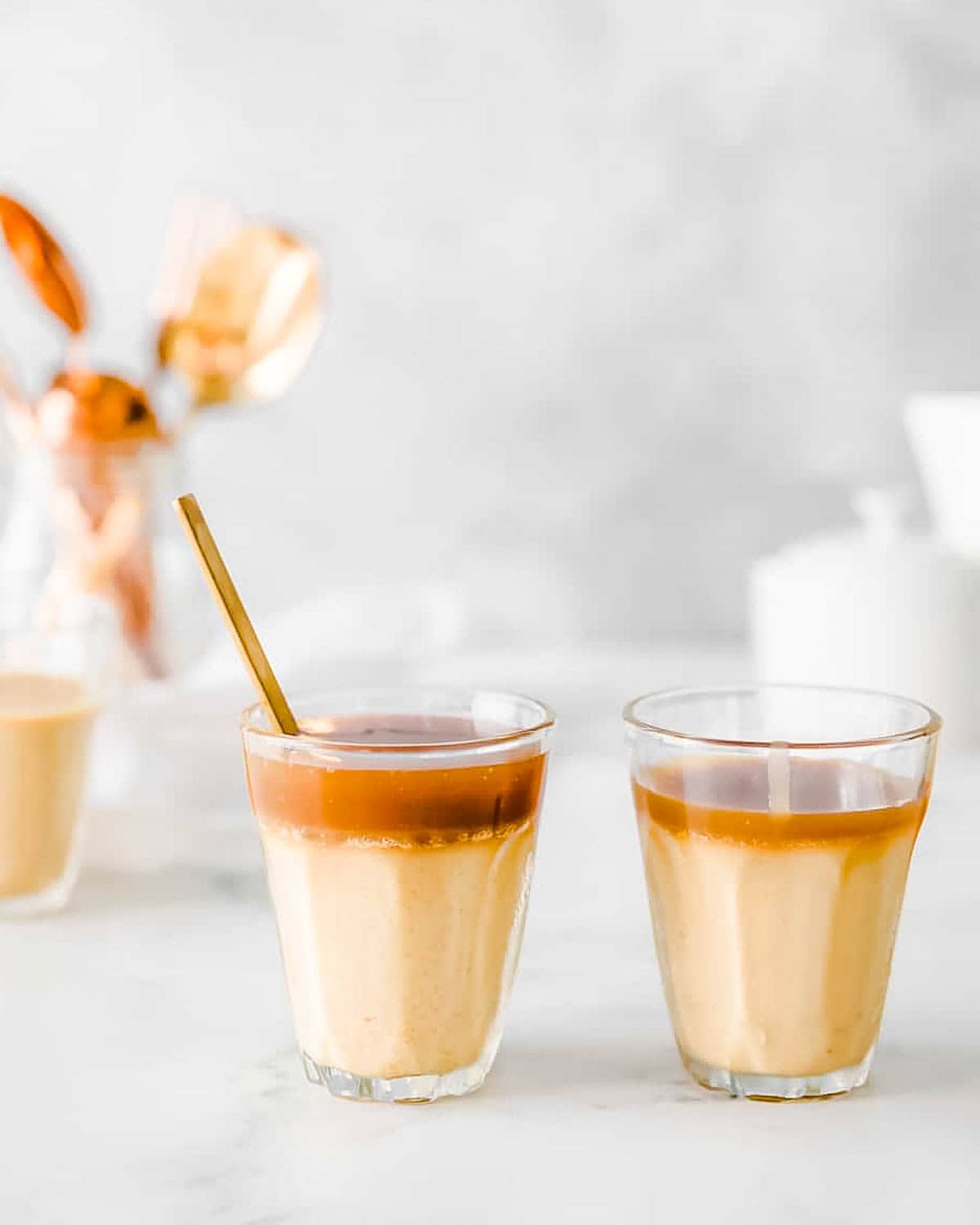 Two glasses of butterscotch budino topped with salted caramel sauce sitting on a marble counter.