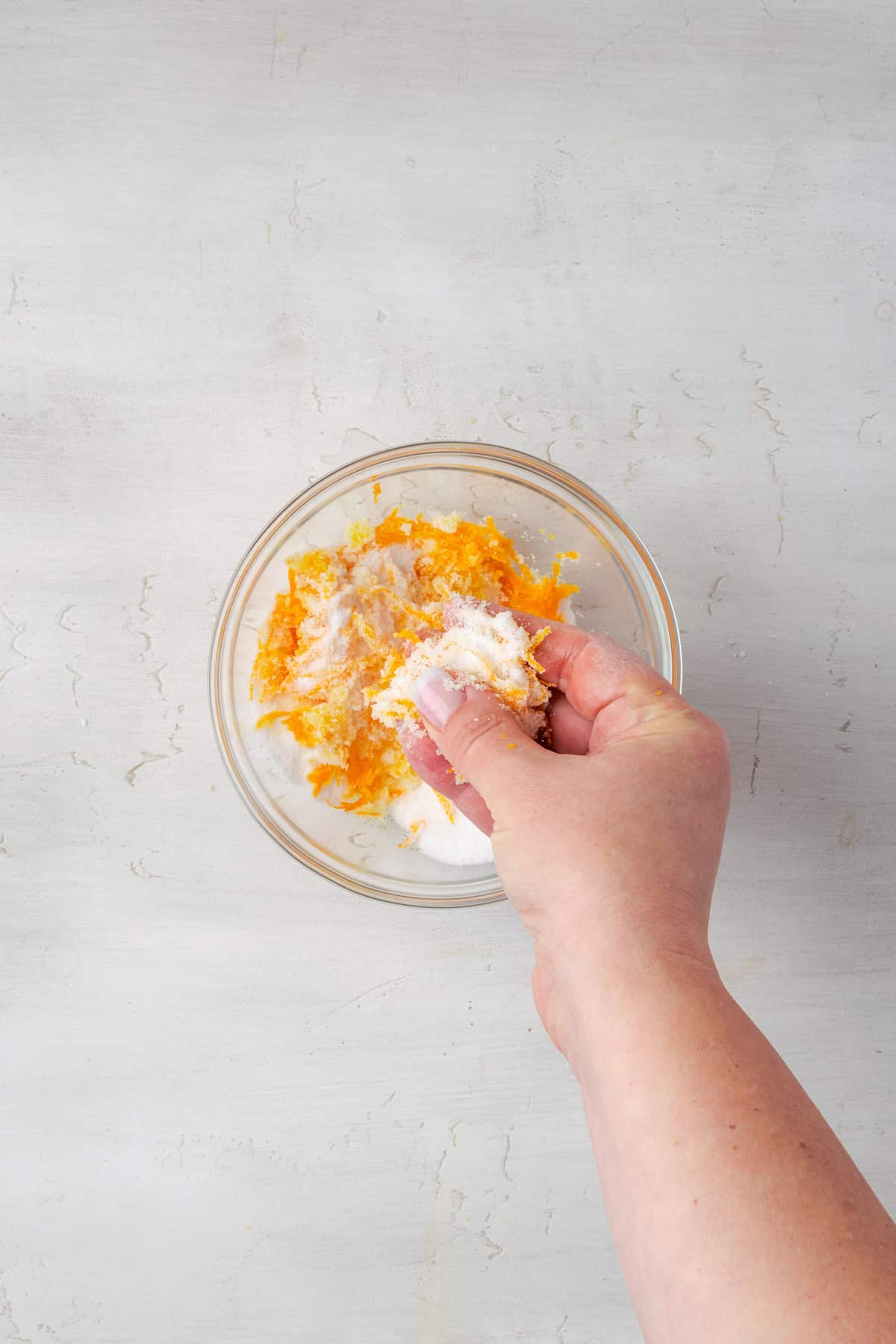 Orange zest being rubbed into granulated sugar in a small bowl. 

