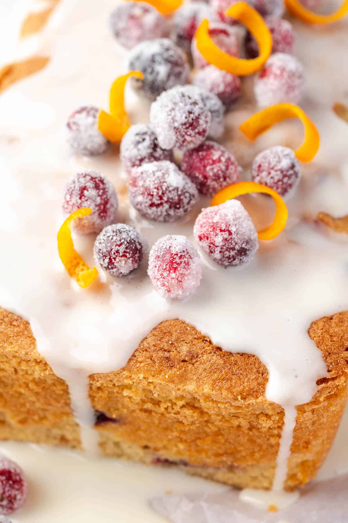 A cranberry orange pound cake topped with orange icing and sugared cranberries.