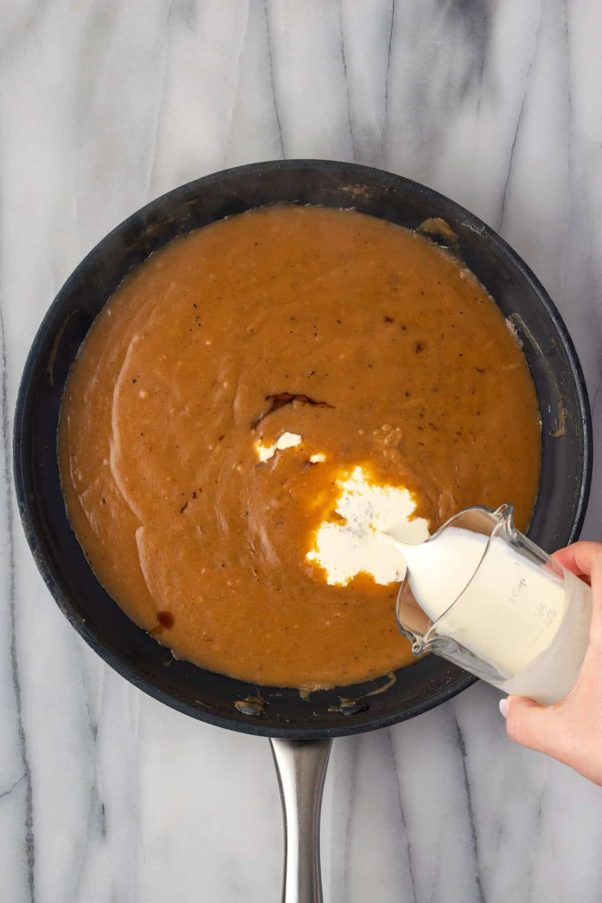 Cream being poured into a beef gravy cooking in a large pan. 