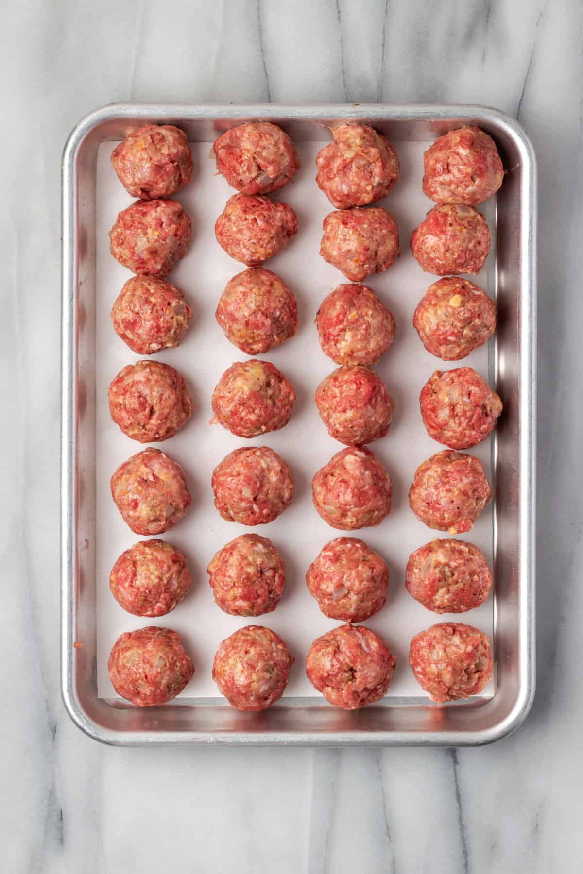 Uncooked meatballs sitting on a baking sheet. 