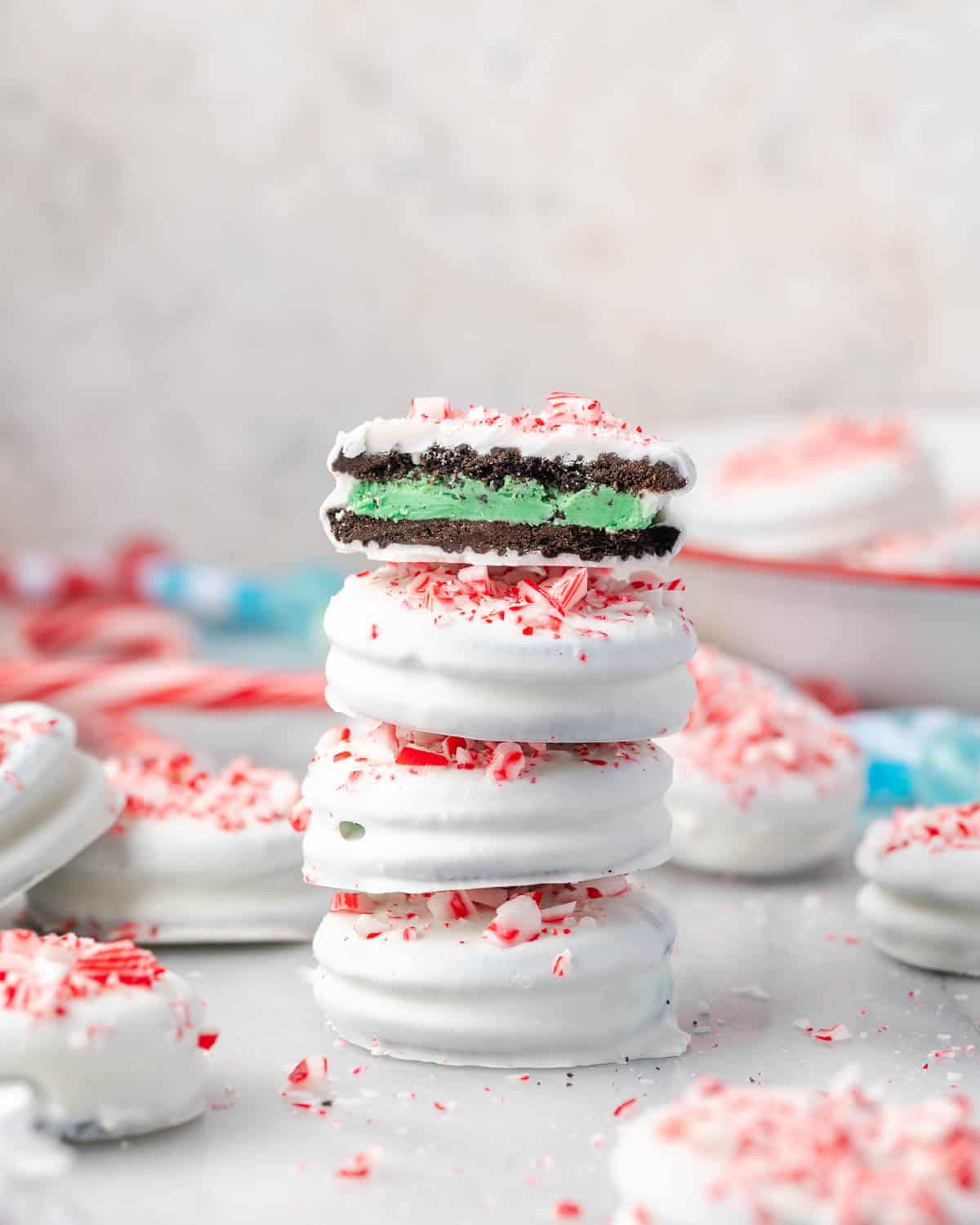 Four Oreo cookies covered with white chocolate and crushed candy canes stacked on a marble counter.