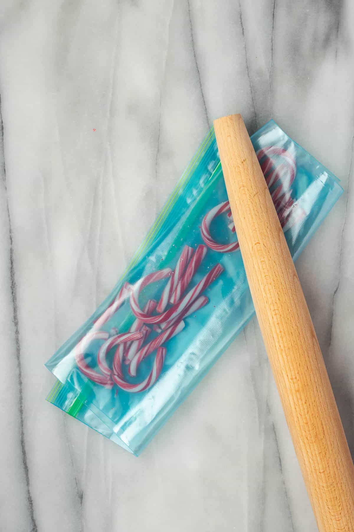 Candy canes inside of a plastic bag being crush with a rolling pin.