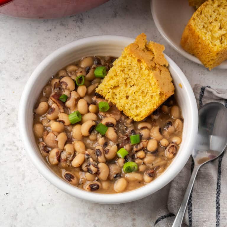 A bowl of black eyed peas garnished with green onion and served with a slice of cornbread.