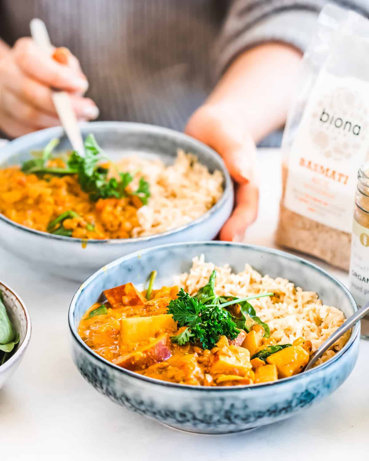 Two bowl of lentil curry served with rice sitting on a countertop. 