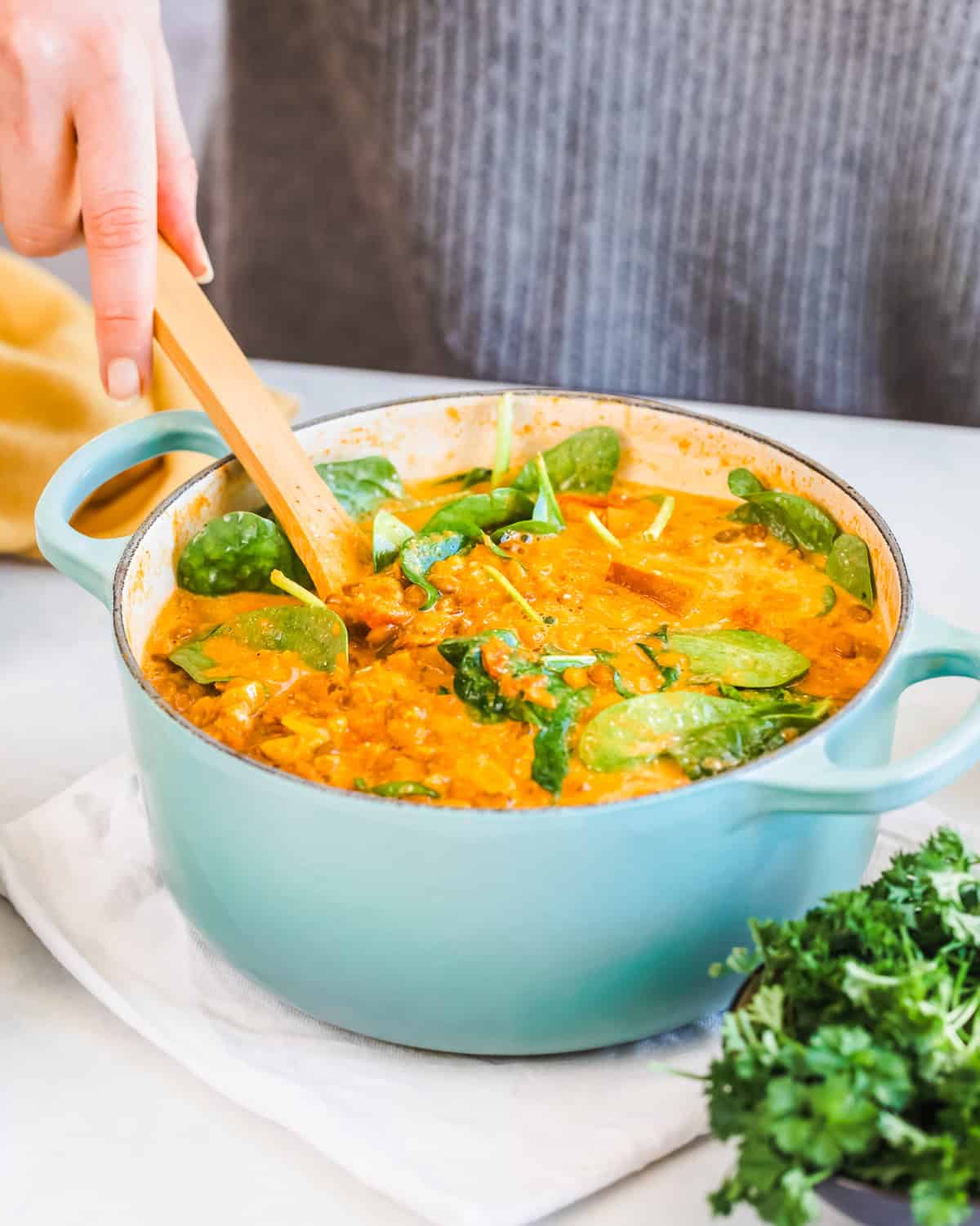 Someone stirring a pot of lentil curry with a wooden spoon. 
