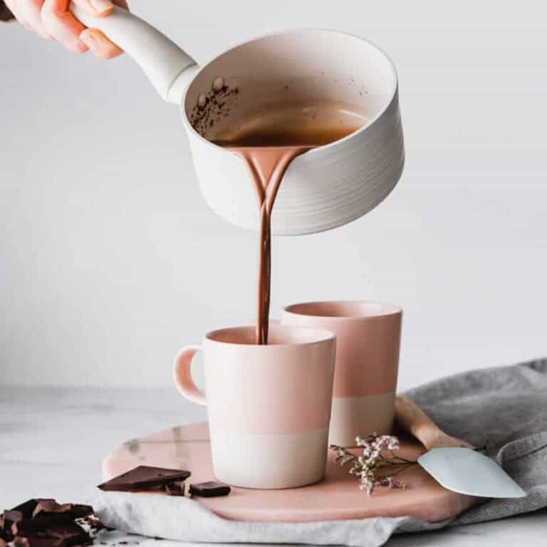 Chai spiced hot chocolate being poured into two mugs.