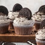 A batch of gluten free cookies and cream cupcakes sitting on a wooden cutting board.