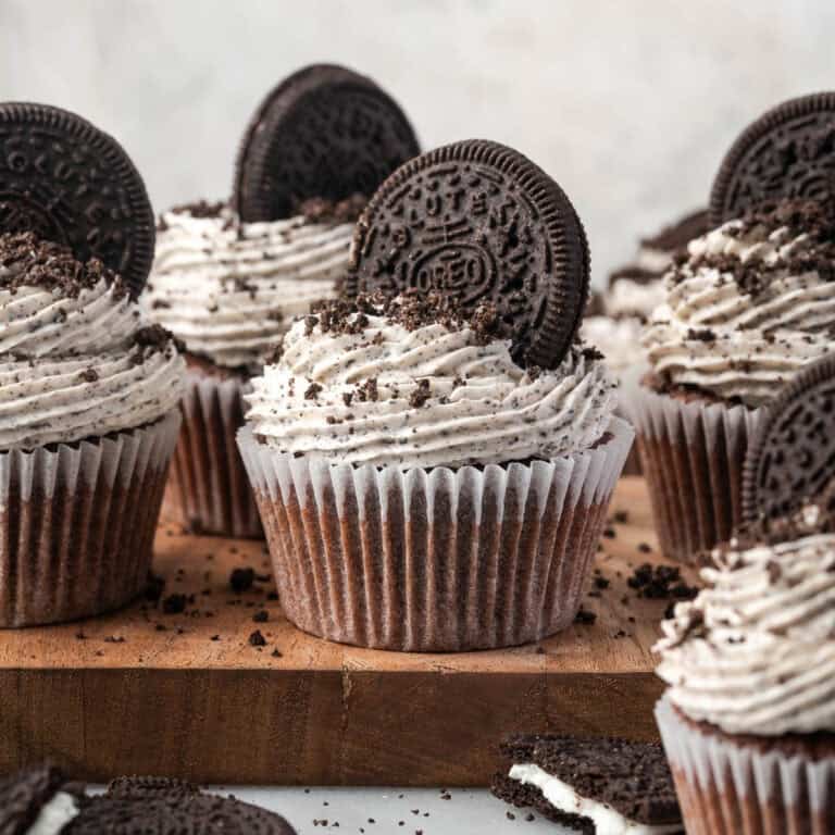 A batch of gluten free cookies and cream cupcakes sitting on a wooden cutting board.