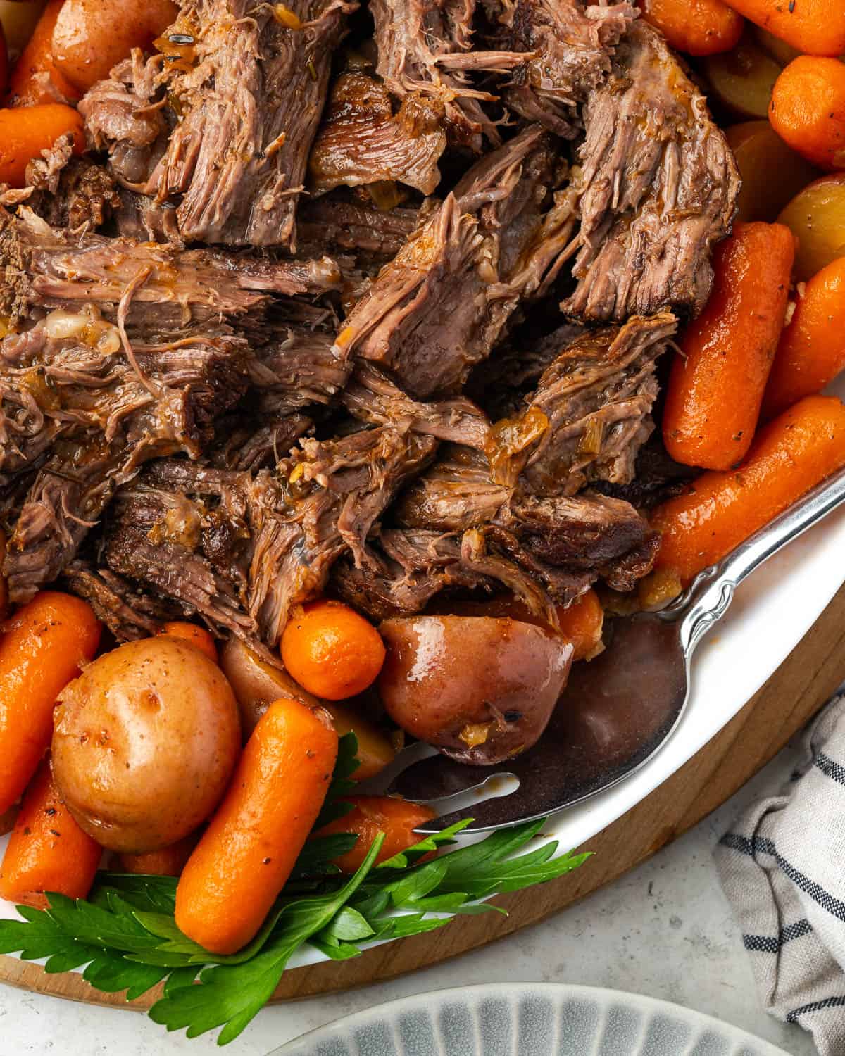 A pot roast pulled into shreds and sitting on a serving platter with potatoes and carrots.