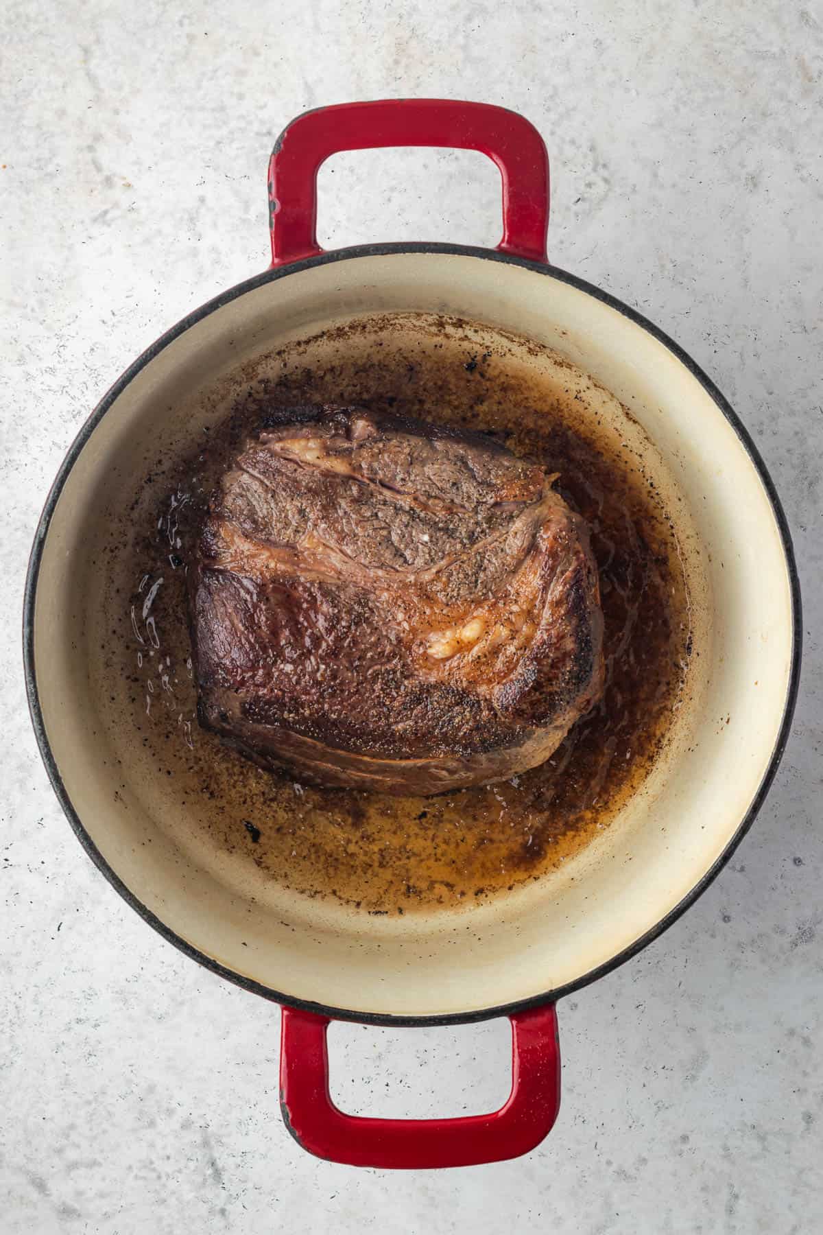 A browned chuck roast sitting in a Dutch oven pot. 