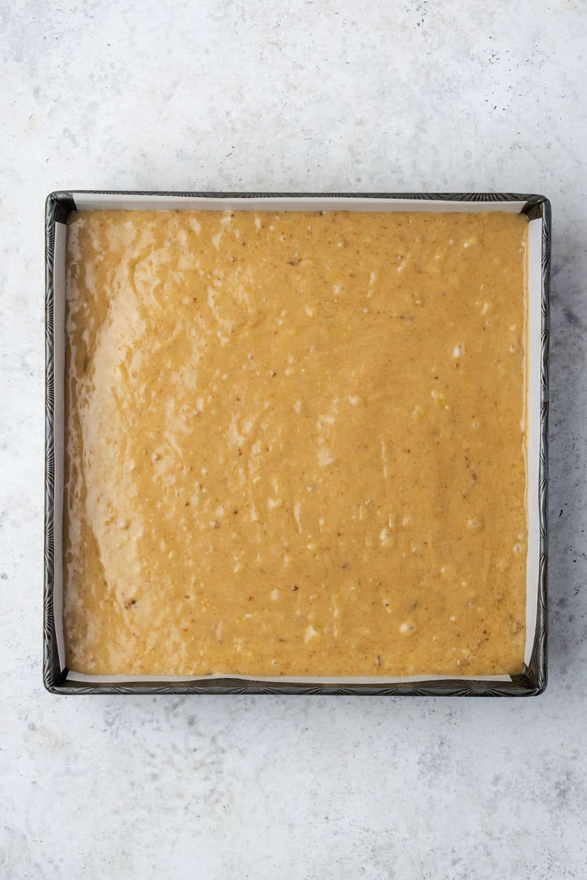 Banana cake batter spread over the bananas and caramel in a square baking pan. 