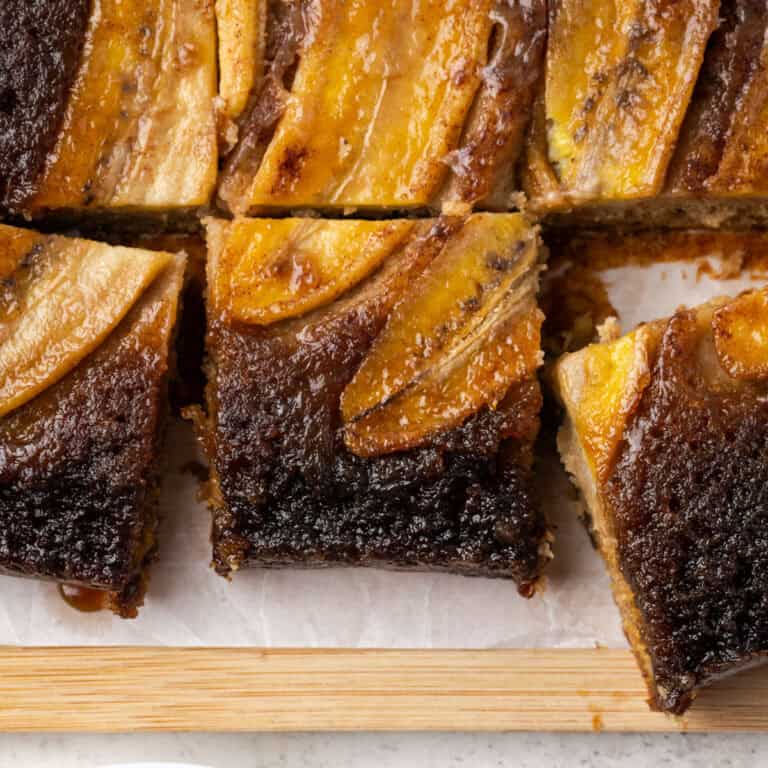 Squares of bananas foster upside down cake sitting on a wood cutting board.