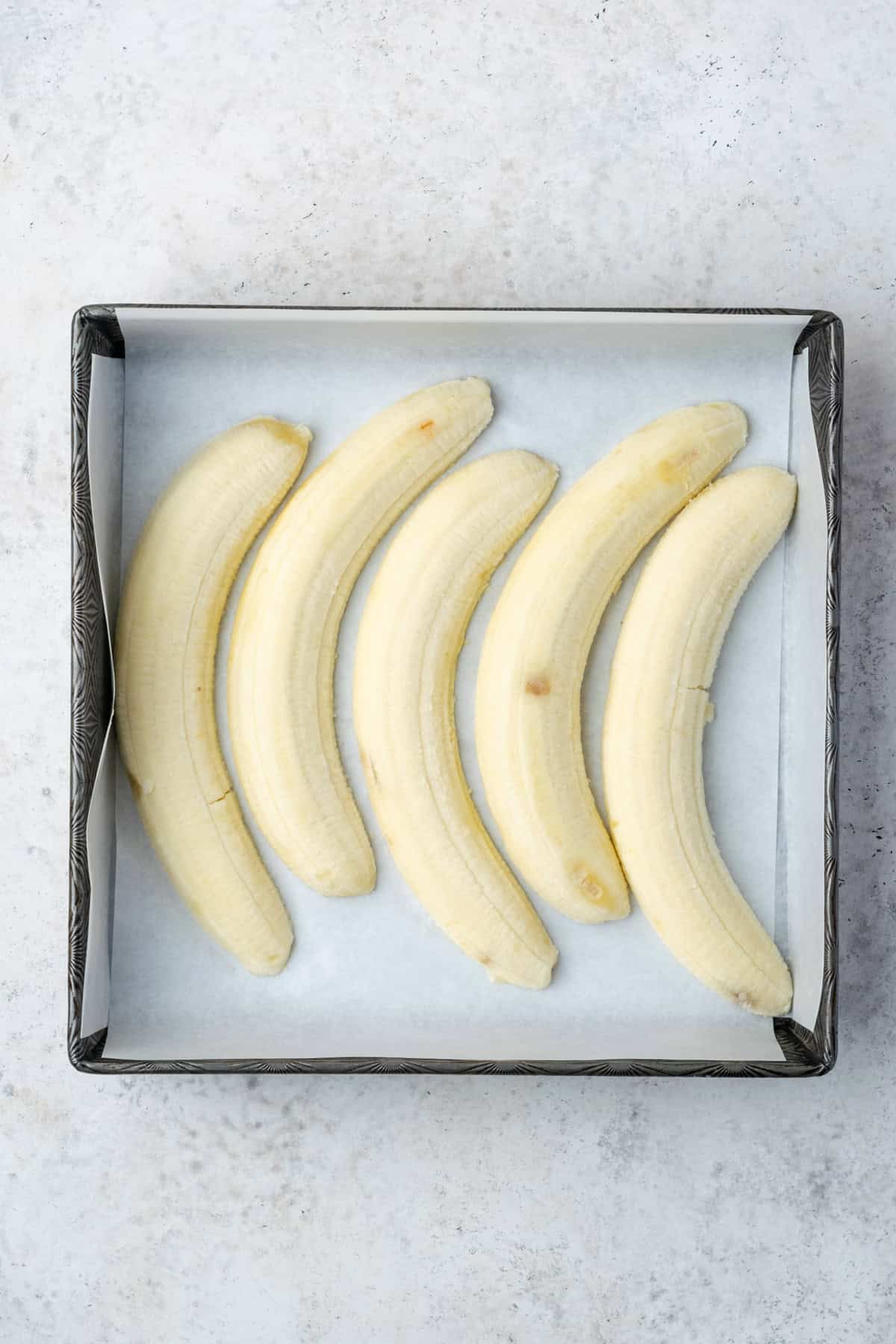 Slices of bananas in the bottom of a square baking pan. 