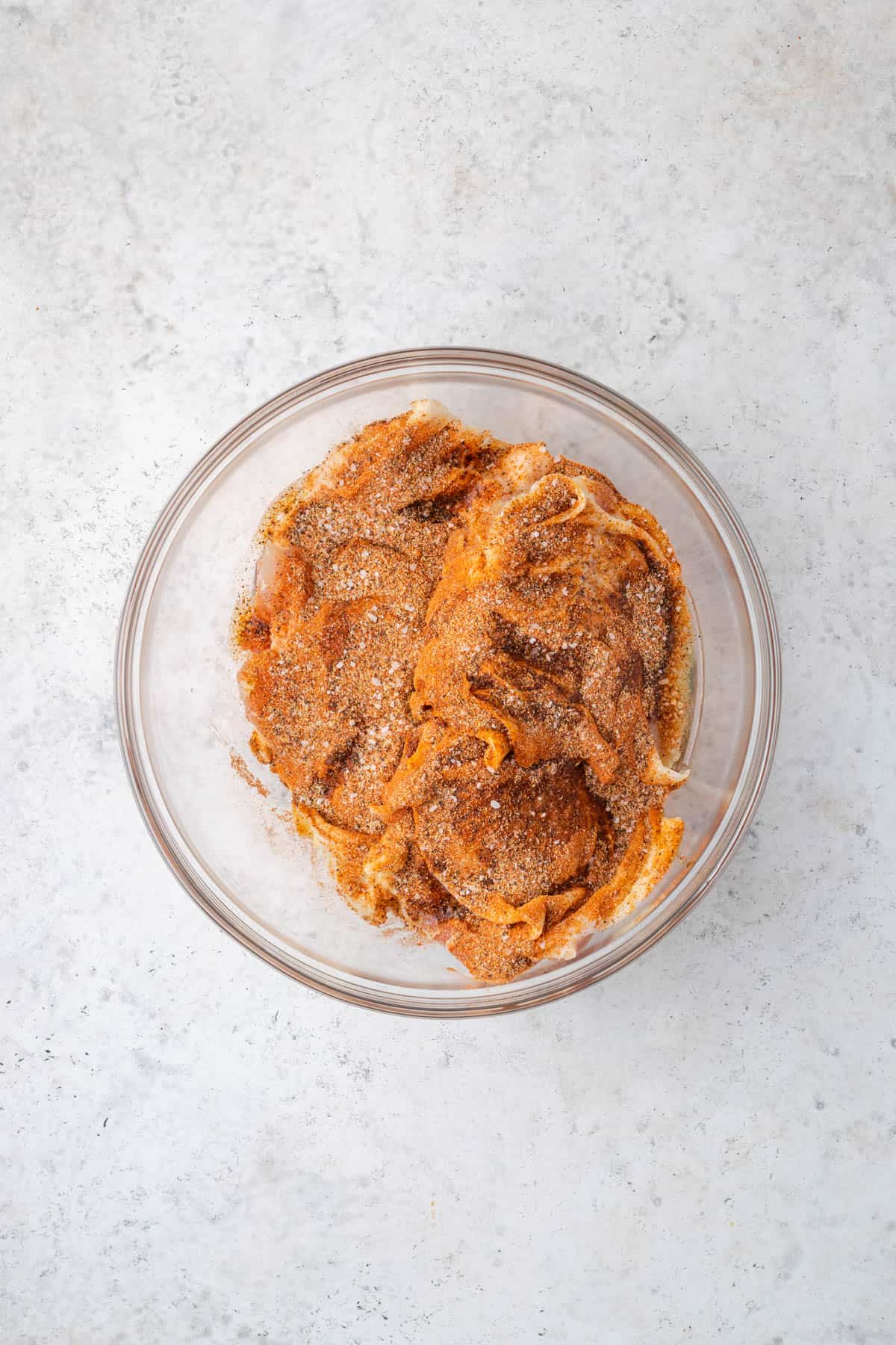 Chicken thighs covered with Cajun seasoning in a large bowl. 
