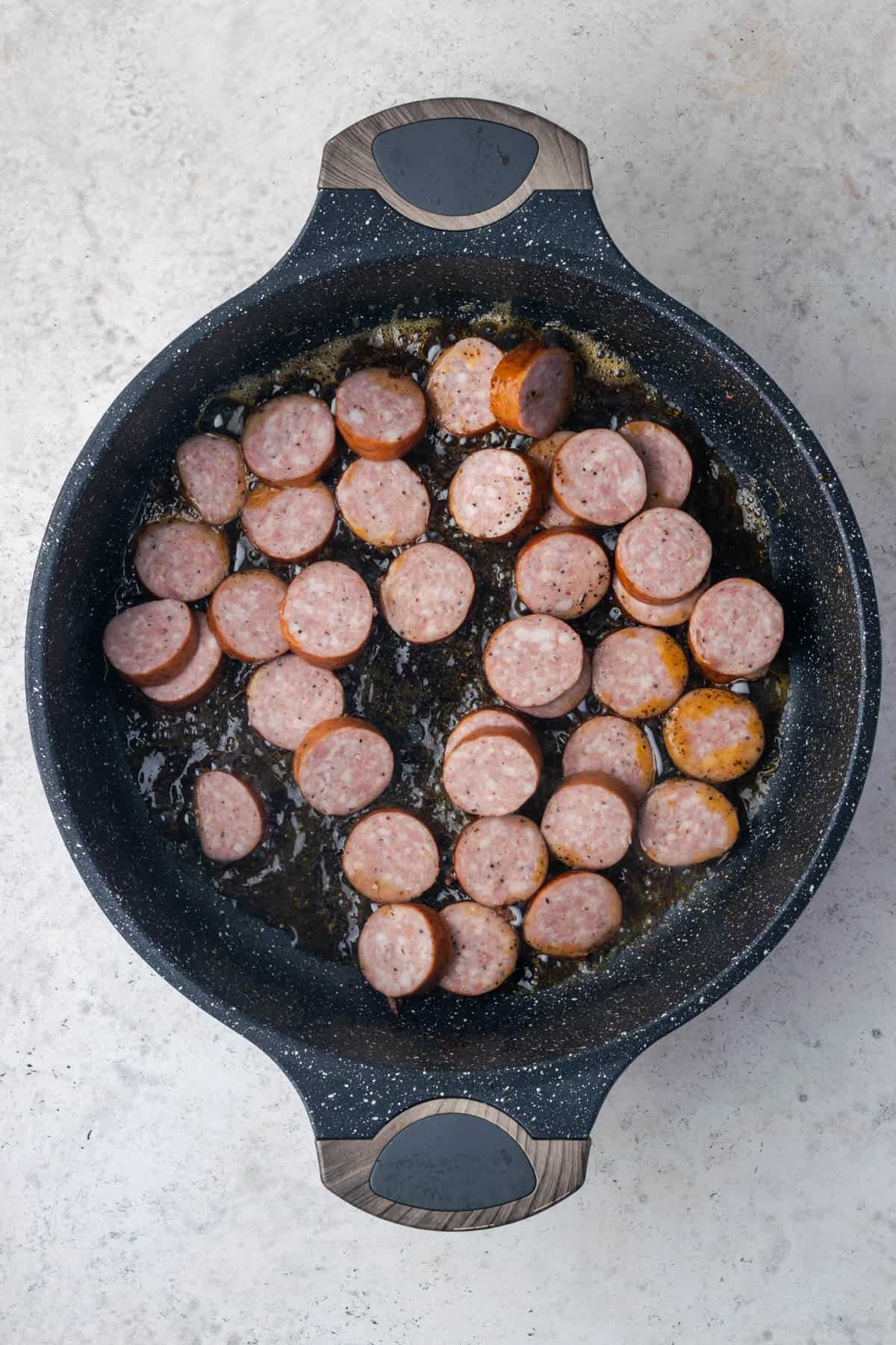 Sliced kielbasa cooking in a large pot. 