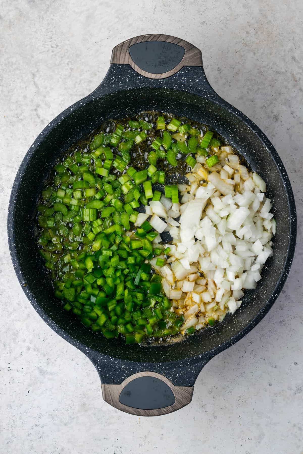 Green bell pepper, onion and celery being sauteed in a large pot. 