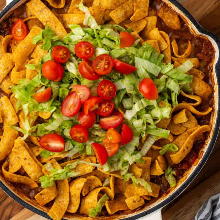 A pan of Frito taco casserole topped with shredded lettuce and tomatoes.