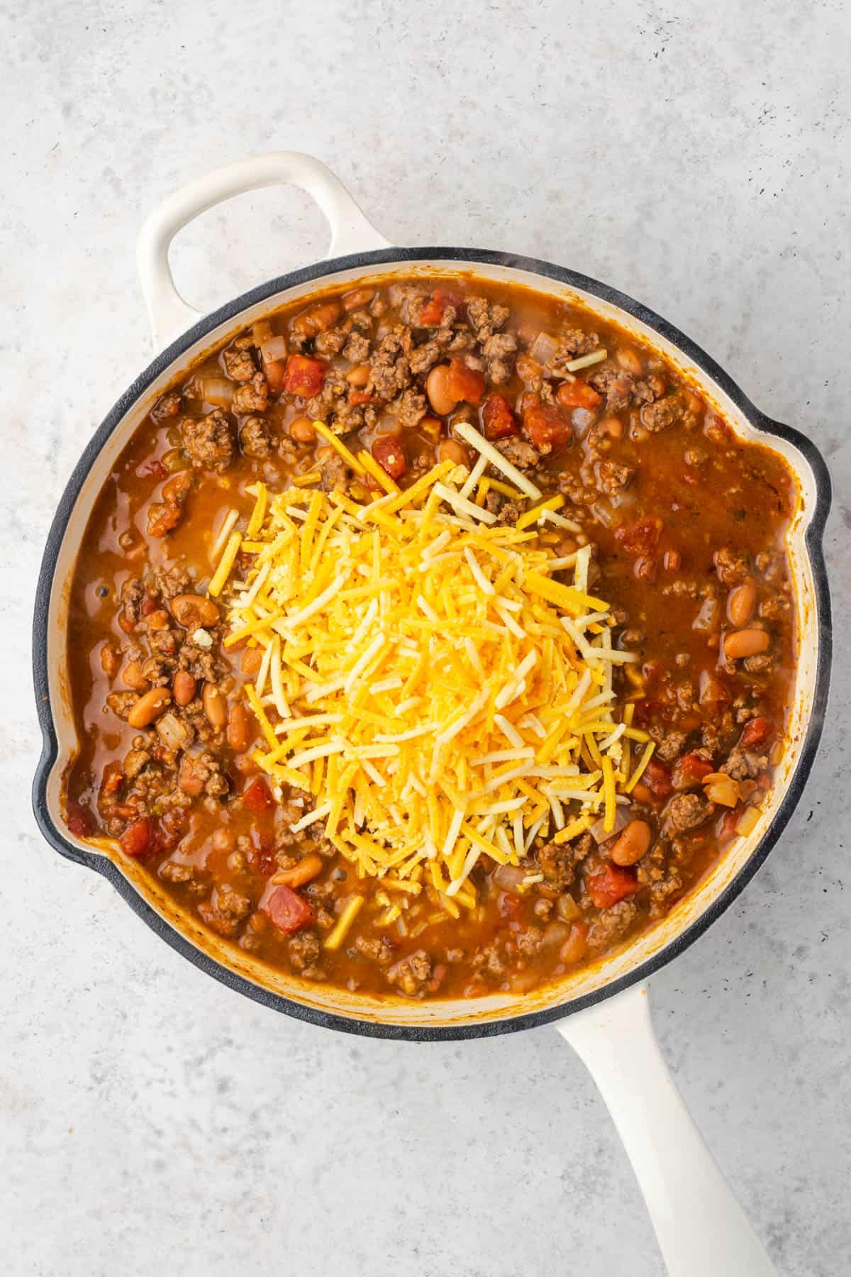 Shredded cheese being mixed into the meat and beans. 