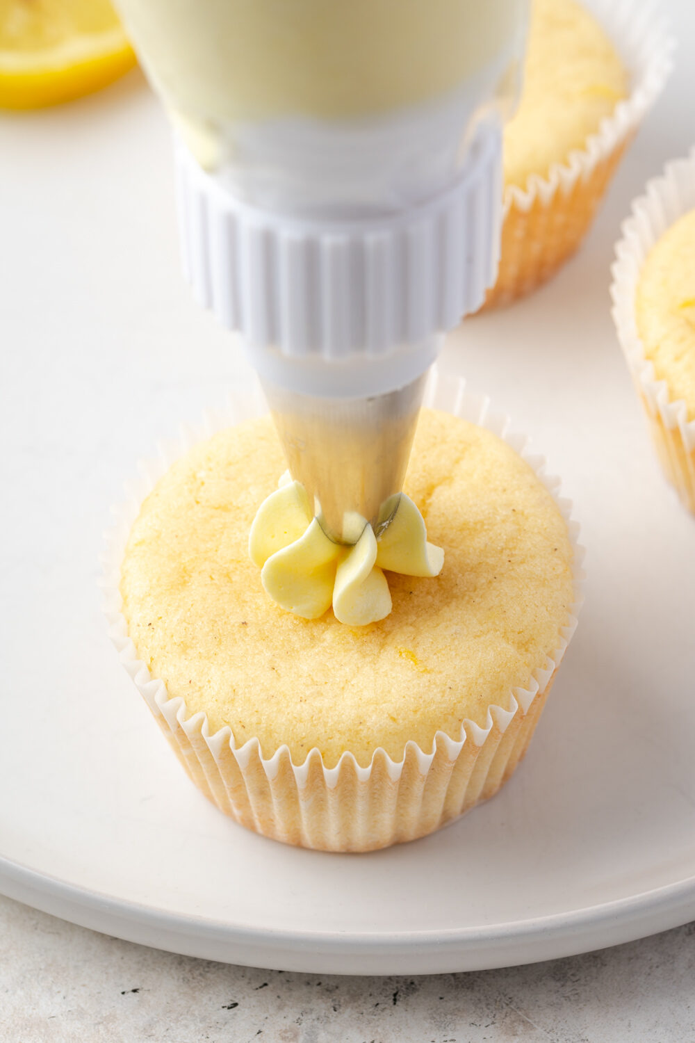 Lemon buttercream frosting being piped on top of lemon cupcakes.