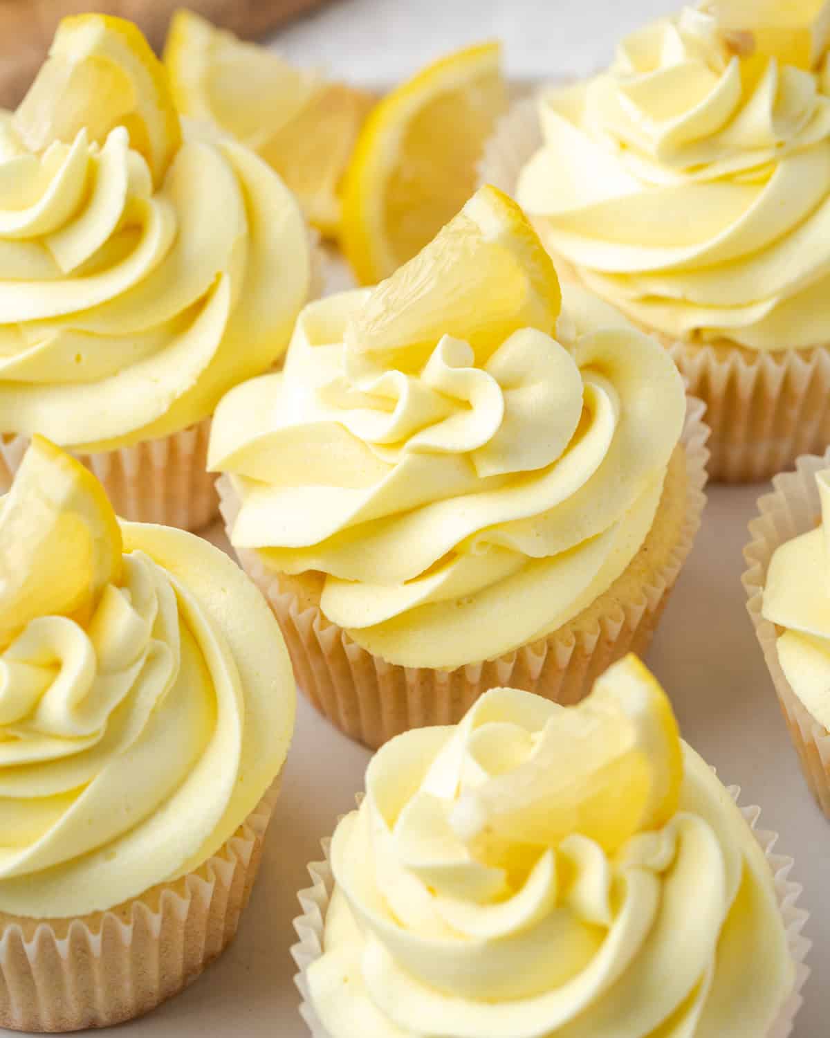 A batch of gluten free lemon cupcakes topped with yellow frosting an a lemon slice sitting on a serving tray.