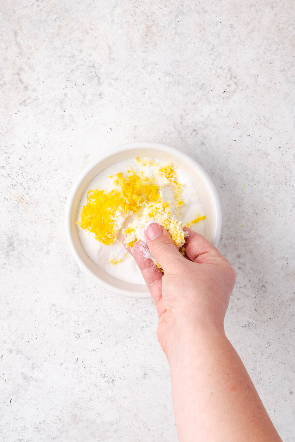 Lemon zest being rubbed into a bowl of sugar.