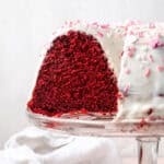 A red velvet bundt cake that has been sliced sitting on a glass cake stand.