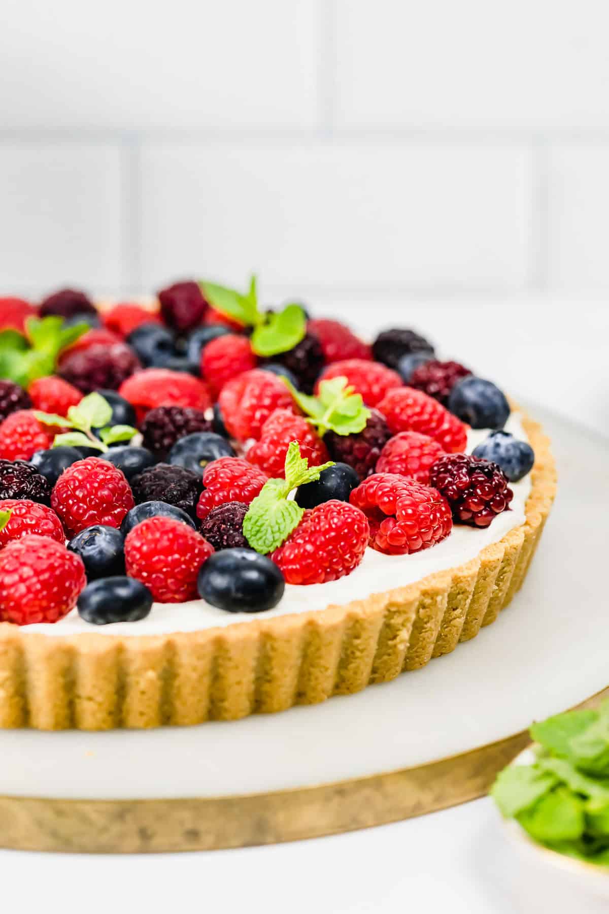 A mixed berry tart topped with raspberries, blueberries, blackberries and fresh mint sitting on a marble tray.